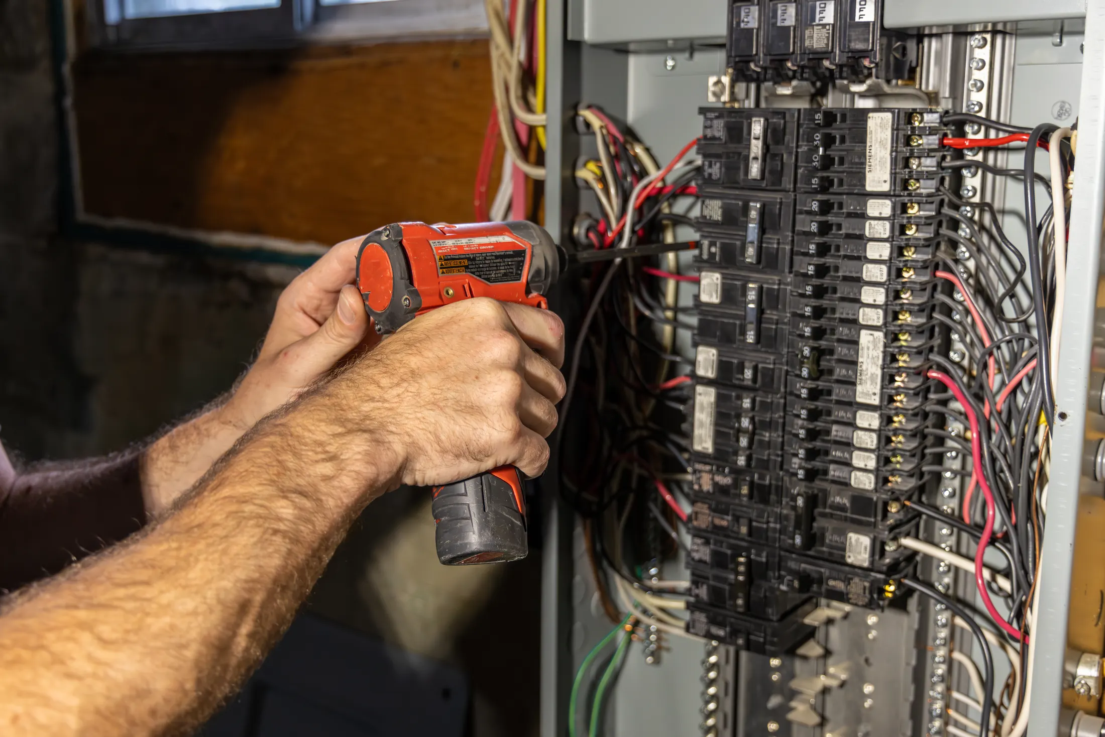 Electrician installing a ground wire in a circuit breaker panel with a power drill