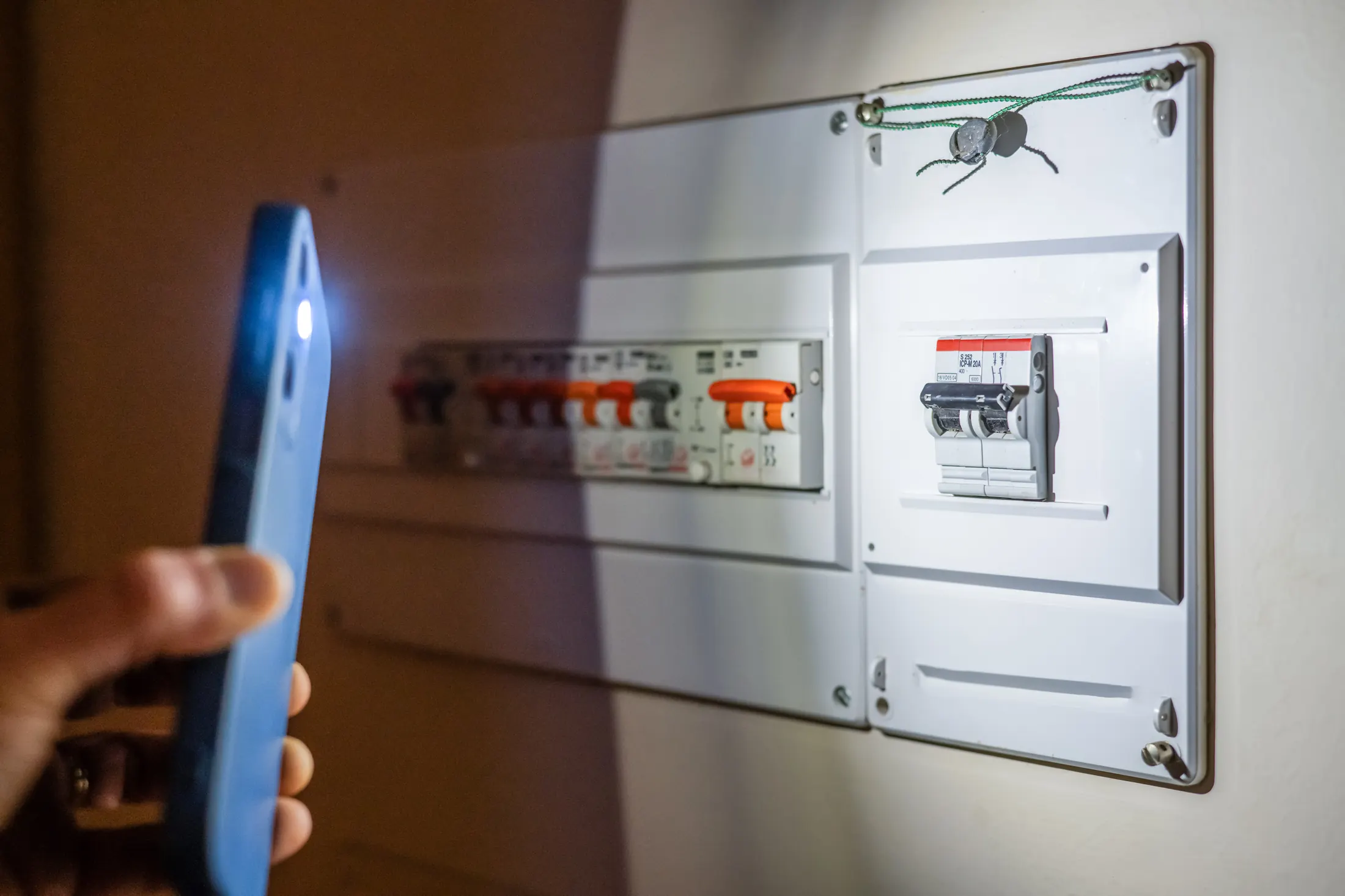 Person using a phone flashlight to check a tripped fuse box during a home power outage